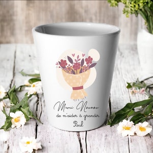Peut inclure: Mug en céramique blanche avec une illustration de bouquet de fleurs et le texte "Merci Nounou de m'aider à grandir Paul".