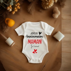 May include: White baby onesie with black text that reads "Joyeux Anniversaire Maman! Je t'aime!" with a black and white heart and three red hearts.