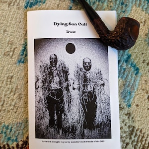 May include: A black and white photo of two people standing in a field of tall grass. The photo is on a white paper with the text "Dying Sun Cult" and "Trust" printed in black. The text "Artwork brought to you by members and friends of the DSC" is printed at the bottom of the page.