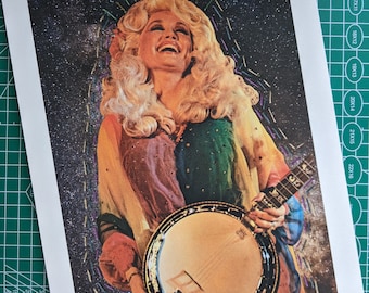 May include: A rectangular art print featuring a portrait of a smiling blonde person with voluminous hair, wearing a multi-colored rainbow-toned garment, and holding a round banjo. The background is a dark, starry space-themed design with glitter.