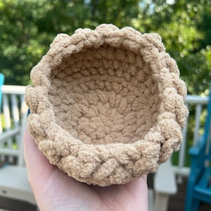 May include: A small, beige crocheted bowl with a textured surface. The bowl is empty and appears to be handmade.