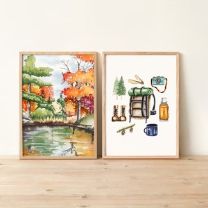 Op de afbeelding: Twee ingelijste aquarellen. De eerste aquarel toont een sc&egrave;ne met een meer en bomen in herfstkleuren. De tweede aquarel toont een verzameling kampeeruitrusting, waaronder een rugzak, laarzen, een thermoskan, een mok en een camera.