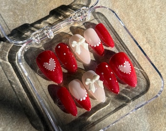 May include: A set of red and white press-on nails with heart and bow designs in a clear plastic case.