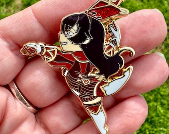 Op de afbeelding: Gouden emaille pin met een cartoonfiguur met zwart haar, een rood-witte outfit en een rode strik. Het personage staat in een dynamische pose met een gestrekt been.
