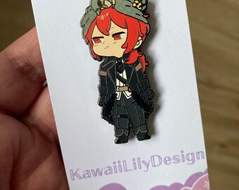 May include: A metal enamel pin featuring a chibi-style character with bright red hair, wearing a dark coat and a grey bird perched on their head. The pin is attached to a white backing card with the text KawaiiLilyDesign printed in purple.
