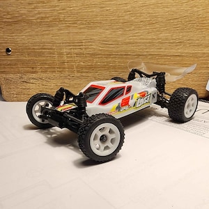 May include: A white and red remote control car with black wheels and a clear plastic spoiler. The car has the word "LOST" printed on the side.