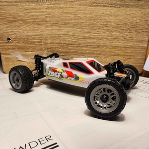 May include: A white, red and yellow remote control car with black wheels and a clear plastic spoiler. The car has the word "LOST" printed on the side.