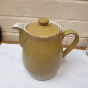 May include: A brown ceramic coffee pot with a lid. The pot has a textured surface and a white rim.