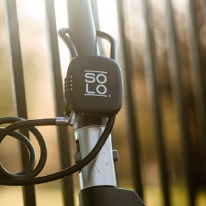 Può includere: Un lucchetto per bicicletta nero con una serratura a combinazione e un cavo. Il lucchetto ha la scritta "SOLO" stampata in bianco.