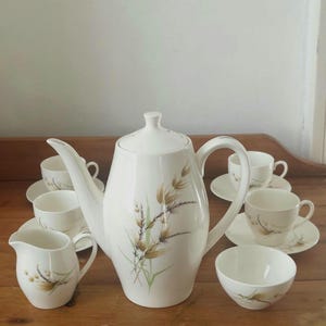 May include: A white tea set with a brown and green floral design. The set includes a teapot, creamer, sugar bowl, and four cups and saucers.