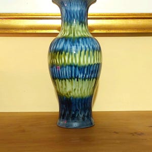 Op de afbeelding: Een blauwe en groene keramische vaas met een gestreept patroon. De vaas staat op een houten oppervlak.