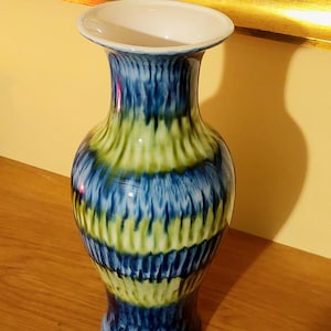 May include: A blue and green ceramic vase with a white interior. The vase has a wide mouth and a narrow base. It is decorated with a swirling pattern of blue and green.