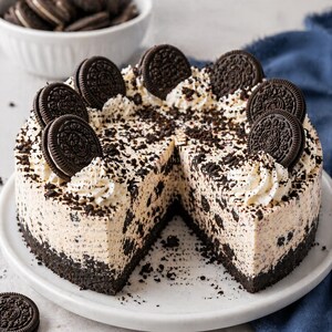 Può includere: Una cheesecake rotonda Oreo con una fetta rimossa, che rivela un interno cremoso con pezzi di biscotti. La torta è decorata con panna montata e biscotti Oreo interi, presentata su un piatto bianco.