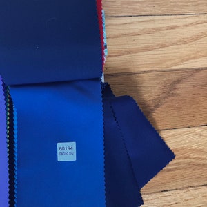 May include: A stack of fabric swatches in various shades of blue, including a dark navy blue, a medium blue, and a light blue. A small white label with the text "60194 pacific blu" is attached to the medium blue swatch.