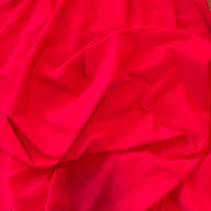 May include: A bright red fabric backdrop, folded and draped, creating soft, flowing folds. The fabric is smooth and wrinkle-free, ideal for photography or videography.