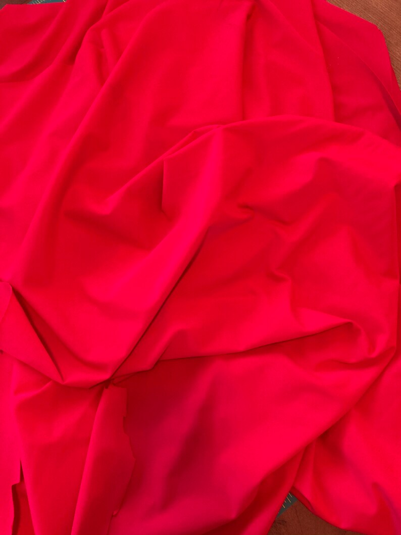 May include: A bright red fabric backdrop, folded and draped, creating soft, flowing folds. The fabric is smooth and wrinkle-free, ideal for photography or videography.