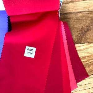 May include: A swatch book of red fabric samples. The top swatch is a bright red and labeled "4186 redcoat".