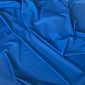 May include: A close-up of a smooth, blue fabric with a soft, drapey texture. The fabric is folded and creased, creating a dynamic visual.