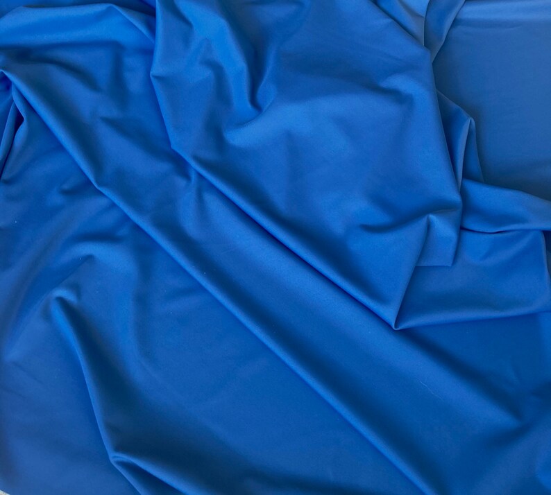 May include: A close-up of a smooth, blue fabric with a soft, drapey texture. The fabric is folded and creased, creating a dynamic visual.