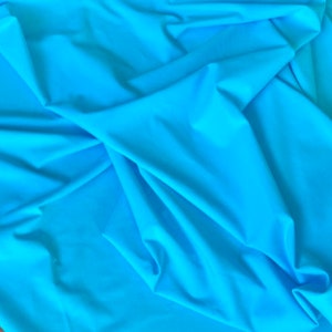 May include: A bright turquoise fabric with a smooth, silky texture. The fabric is folded and draped, showcasing its flowing nature.