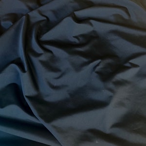 May include: A close-up of a black fabric with a smooth, silky texture. The fabric is folded and draped, showing its soft and flowing nature.