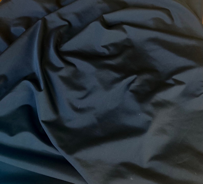 May include: A close-up of a black fabric with a smooth, silky texture. The fabric is folded and draped, showing its soft and flowing nature.