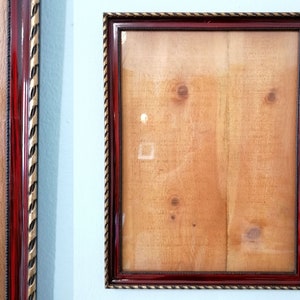 Può includere: Una cornice per foto rossa con una bordura dorata. La cornice è vuota e ha una texture simile al legno.