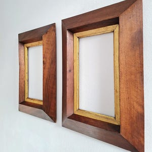 May include: Two rectangular picture frames featuring a wide, dark brown wooden outer border with a beveled edge and a thin, metallic gold inner trim. The frames are empty, showcasing a clean, angled design that highlights the contrast between the wood.