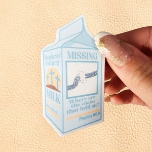 Puede incluir: Una pegatina azul claro con forma de cartón de leche. La pegatina tiene las palabras "MISSING" y "MILK", junto con el texto "Where are the chains that held me? Psalms 107:14".