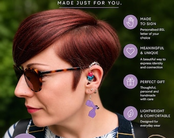 Può includere: Orecchini BSL personalizzati con una forma di mano viola in un gesto della lingua dei segni. Gli orecchini sono indossati sul lobo, completati da un ear cuff argentato con perline rosa e blu. L'immagine include il testo: Wear Your Language. Celebrate BSL.