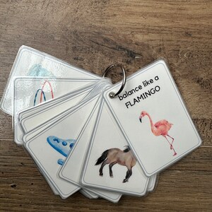K&ouml;nnte beinhalten: Ein Satz von Karteikarten mit Bildern und Text. Die Karten werden mit einem Metallring zusammengehalten. Eine Karte zeigt einen Flamingo mit dem Text "balance like a FLAMINGO".