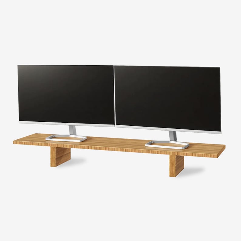 May include: Two black computer monitors with silver stands sit on a light brown wooden monitor stand. The stand has a rectangular top and two supporting legs. The monitors are side-by-side.