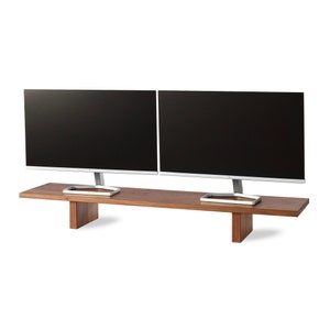 May include: A dual monitor stand made of dark wood, with two computer monitors. The monitors have black screens and silver stands. The stand is rectangular with two supporting legs.