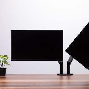 Peut inclure: Deux moniteurs d'ordinateur noirs montés sur un bureau avec un support noir. Les moniteurs sont positionnés côte à côte, le moniteur gauche étant légèrement plus haut que le moniteur droit.