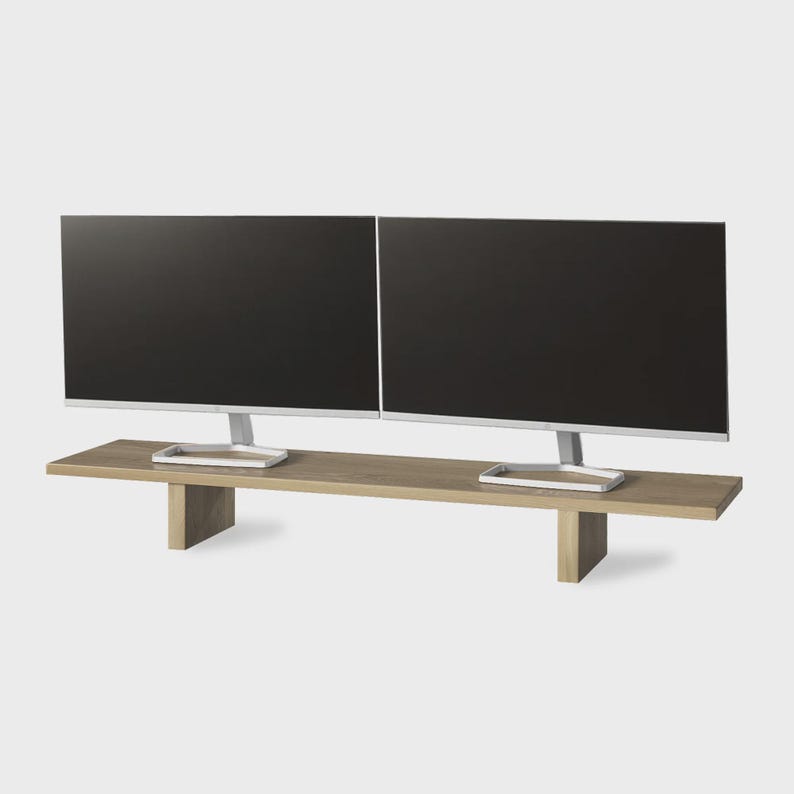 May include: Two black computer monitors on a light brown wooden desk. The desk has a rectangular top and two supporting legs. The monitors have silver stands.