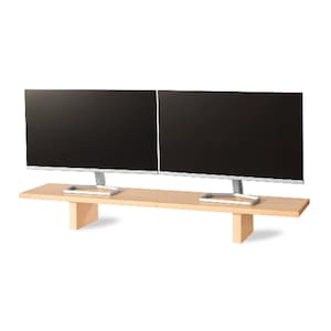 May include: Two black computer monitors with silver stands are placed on a light brown wooden monitor stand. The stand has a rectangular shape with two supporting legs. The monitors are side by side.