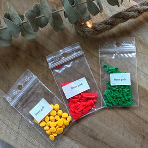 May include: Three small bags of colorful sprinkles. The bags are labeled "Neon gelb", "Neon pink", and "Neon gr&uuml;n".