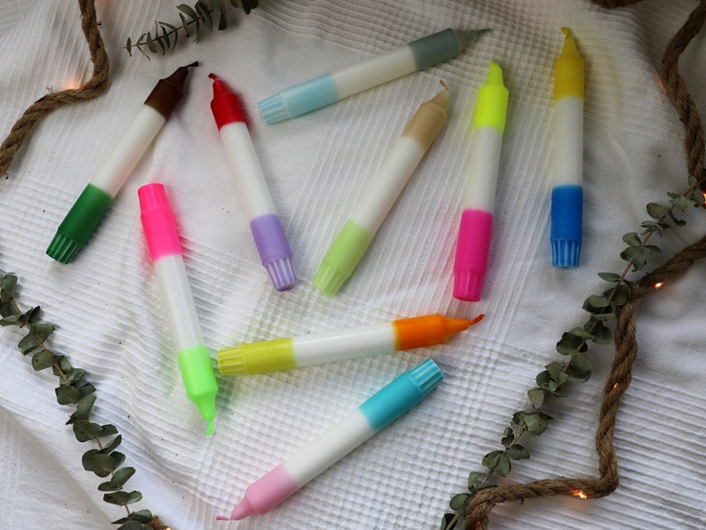 May include: Assortment of colorful candles with a white base. The candles are two-toned with a variety of colors including green, red, pink, blue, yellow, and orange.