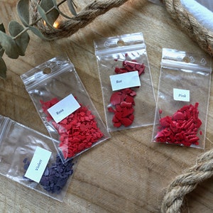 May include: Four small bags of red and purple heart-shaped sprinkles. The bags are labeled "Rosa", "Rot", "Pink", and "Violet".