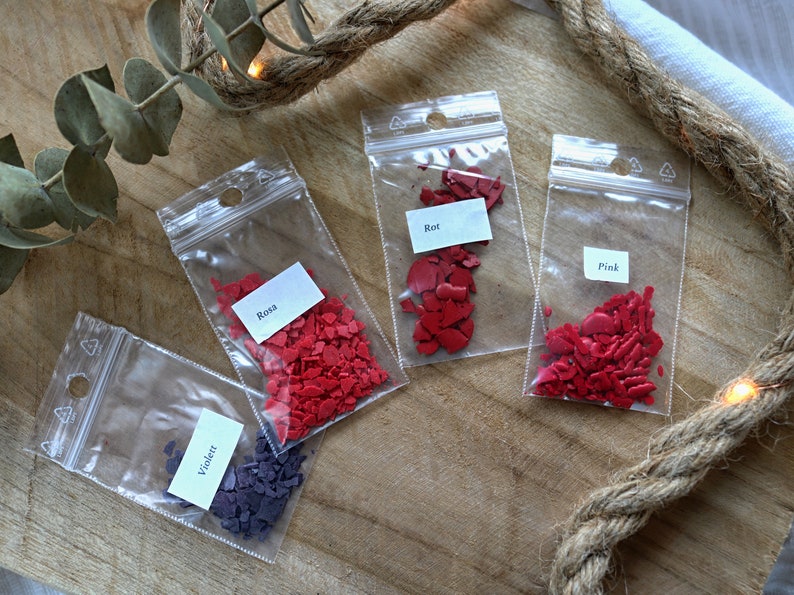 May include: Four small bags of red and purple heart-shaped sprinkles. The bags are labeled "Rosa", "Rot", "Pink", and "Violet".