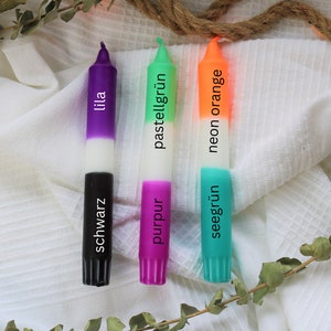 May include: Three candles with different colored wax and labels. The candles are labeled "lila", "pastellgr&uuml;n", and "neon orange". The bottom of each candle is labeled with the color of the wax in German: "schwarz", "purpur", and "seegr&uuml;n".