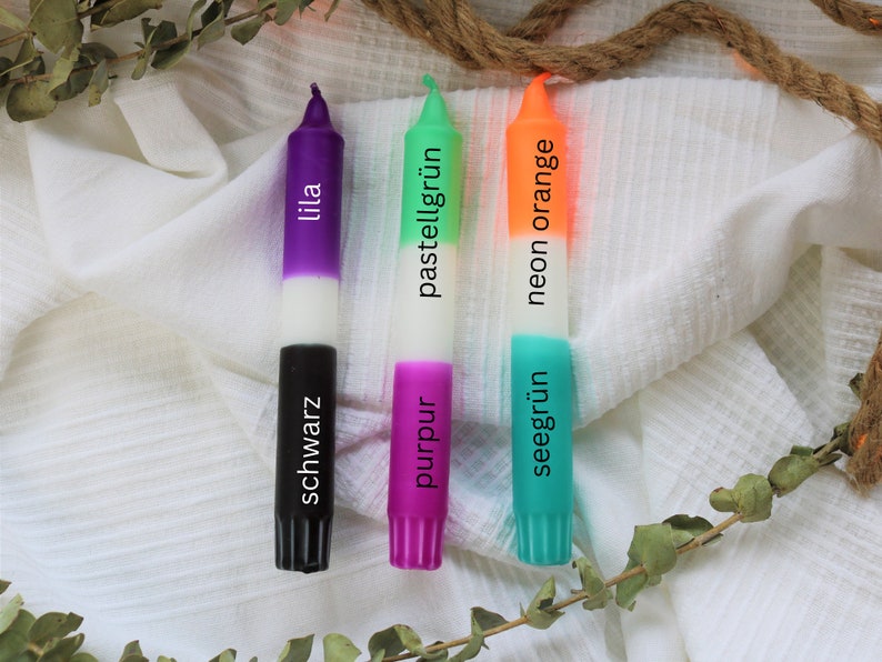 May include: Three candles with different colored wax and labels. The candles are labeled "lila", "pastellgr&uuml;n", and "neon orange". The bottom of each candle is labeled with the color of the wax in German: "schwarz", "purpur", and "seegr&uuml;n".