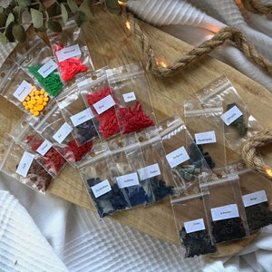 May include: Assortment of small plastic bags filled with colorful sprinkles. The bags are labeled with the color of the sprinkles inside, such as "Red", "Orange", "Yellow", "Green", "Blue", "Black", and "Brown".