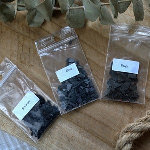 May include: Three small plastic bags containing black, gray, and beige mica powder. The bags are labeled "Schwarz", "Grau", and "Beige".