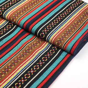 Op de afbeelding: Gestroomde stof met een geweven patroon in tinten bruin, rood, blauw en geel. De stof heeft een textuur en is doormidden gevouwen.