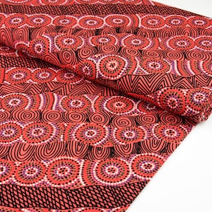 May include: Red fabric with a black and white patterned design featuring circles and dots. The pattern is reminiscent of Aboriginal art.