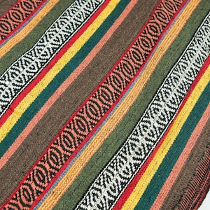 Op de afbeelding: Close-up van een geweven textiel met een streepjespatroon. Het ontwerp heeft afwisselende banden van kleuren, waaronder bruin, groen, geel, rood en wit, met geometrische patronen. Het textiel heeft een getextureerde uitstraling.