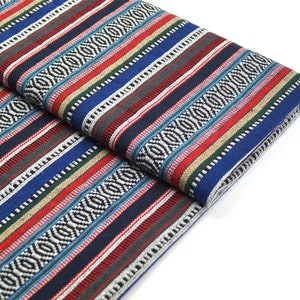 Op de afbeelding: Gestroomde stof met een geometrisch patroon in tinten blauw, rood, wit, zwart en groen. De stof is dubbelgevouwen, waardoor het patroon aan beide kanten zichtbaar is.