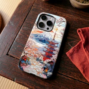 May include: A smartphone case featuring a Japanese-inspired design. The case showcases a pagoda, Mount Fuji, and cherry blossoms in a stained-glass style. The color palette includes shades of blue, red, orange, and white.
