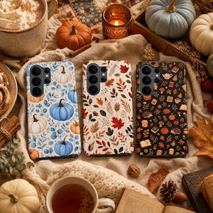 Può includere: Tre cover per smartphone con distinti motivi a tema autunnale. La cover a sinistra mostra zucche blu e arancioni con fogliame. Quella centrale mostra varie foglie autunnali colorate. Quella a destra presenta uno sfondo scuro con icone.